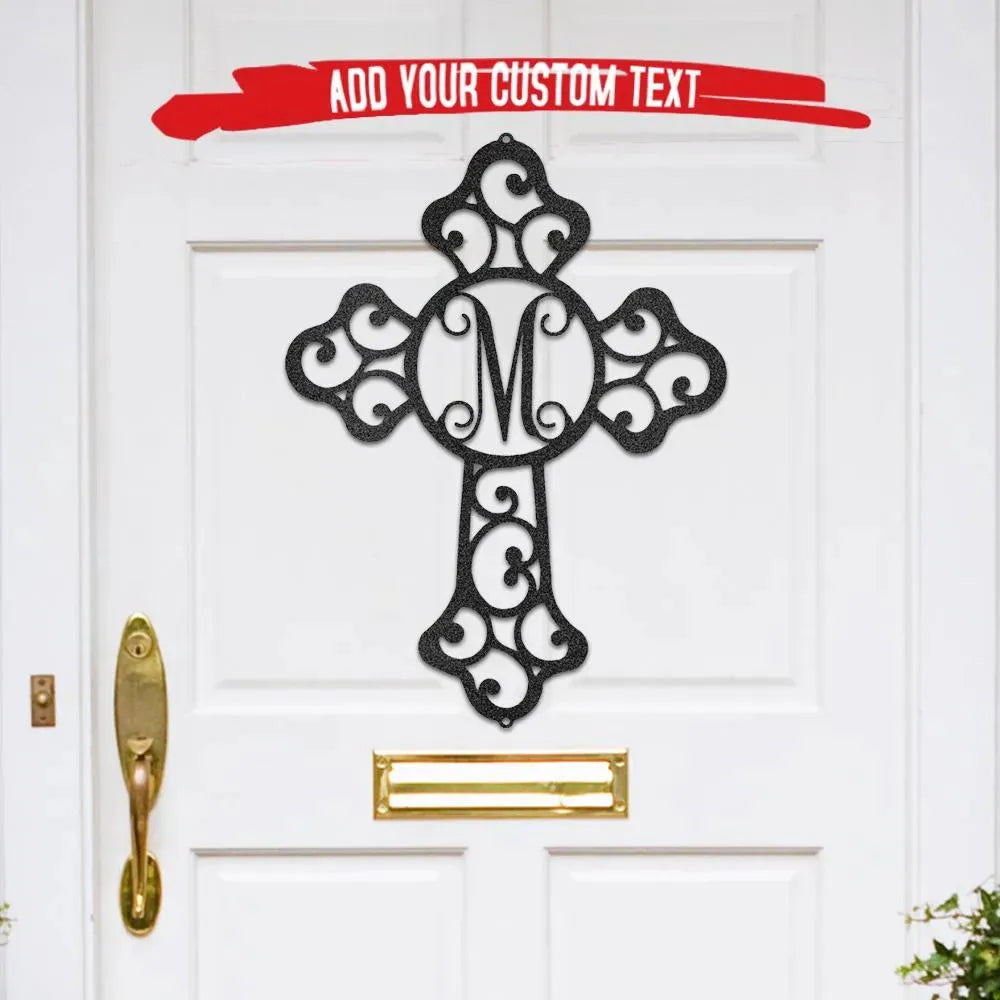 Black metal cross monogram wall art with ornate scrollwork and initial "M" on a white door.