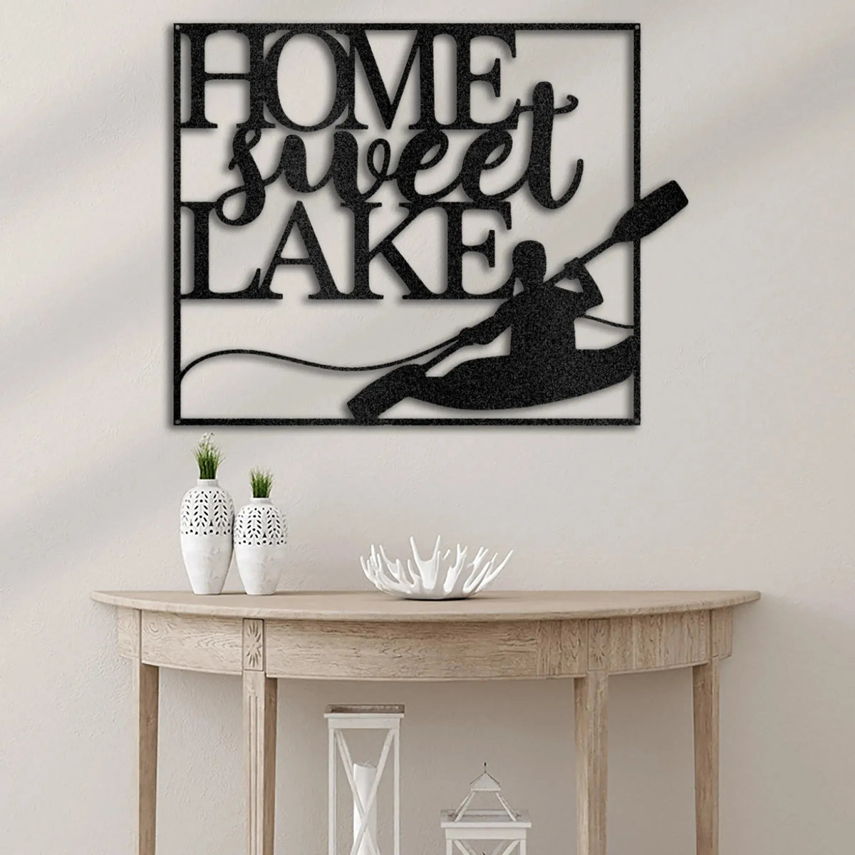 Black metal "Home Sweet Lake" wall art with a kayaker design, displayed above a wooden console table.