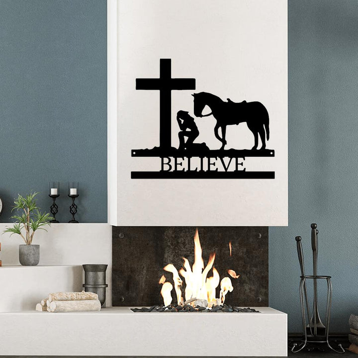 Black metal wall art featuring a kneeling cowgirl, horse, cross, and "BELIEVE" text above a fireplace.