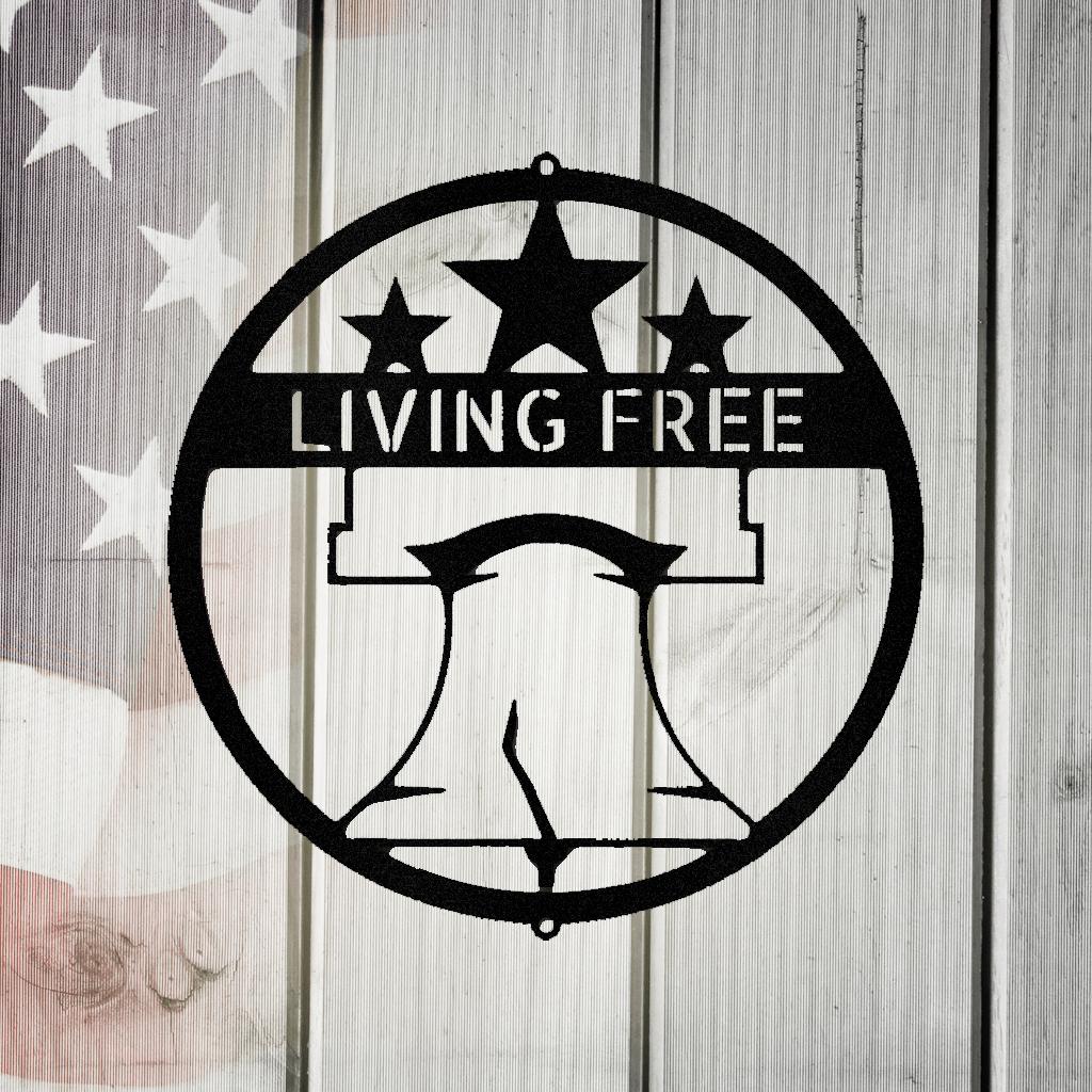 Black metal Liberty Bell monogram wall art with "LIVING FREE" text and stars, on a rustic American flag background.
