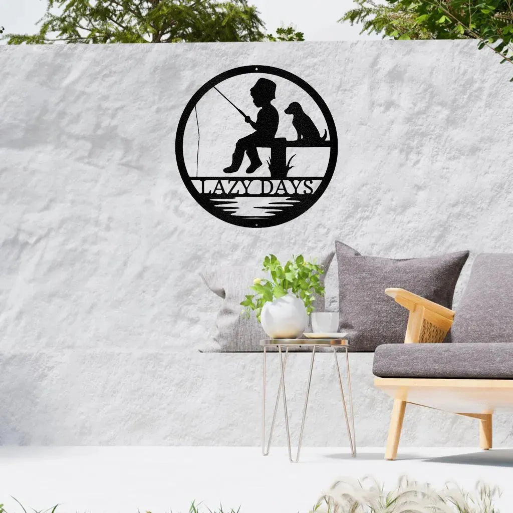 Black metal wall art: boy fishing with dog, "LAZY DAYS" text, circular design.