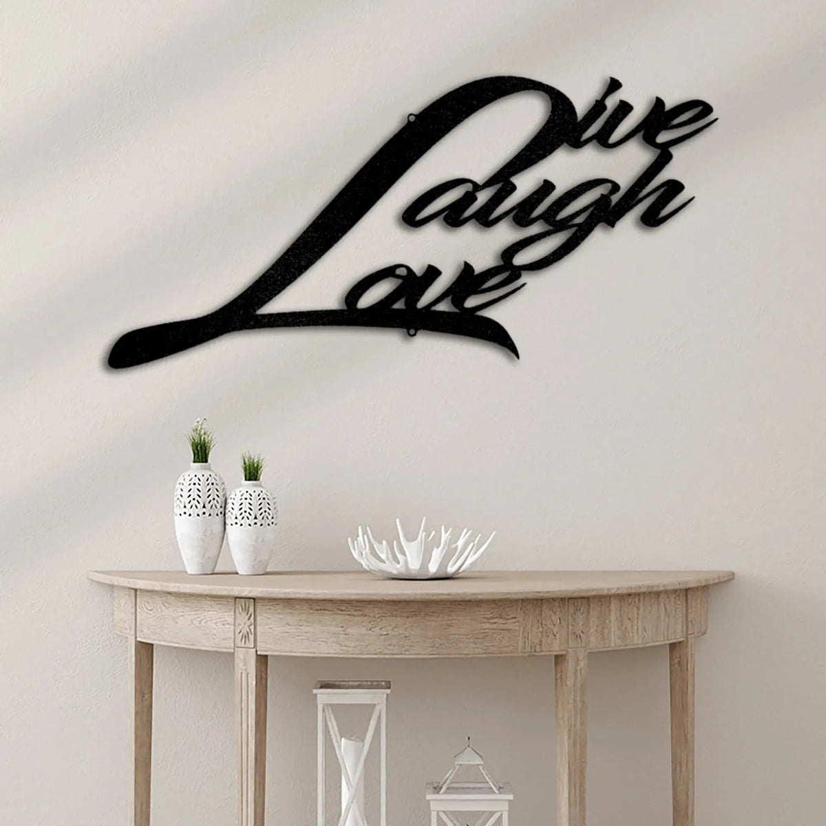 Black metal "Live Laugh Love" script wall art above a wooden console table with white vases.