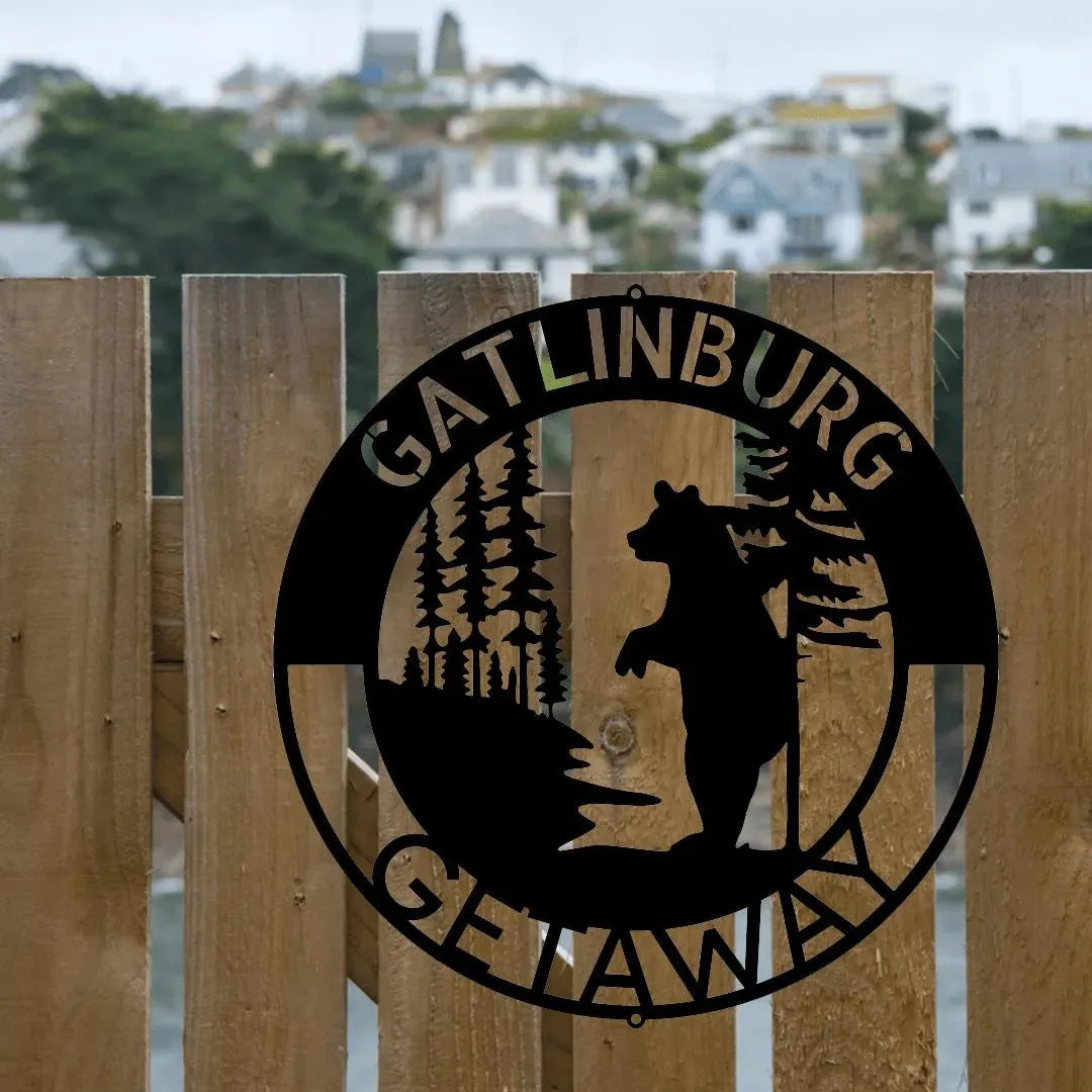 Black metal wall art: "Gatlinburg Getaway" text, bear, and pine trees in a circular design on a wooden fence.
