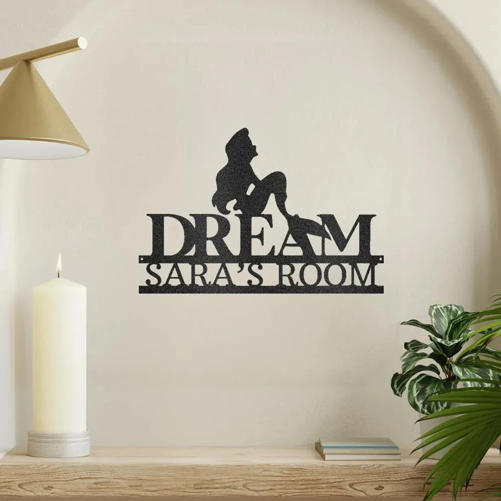 Black metal "DREAM SARA'S ROOM" wall art with a mermaid silhouette, on a shelf with a candle.
