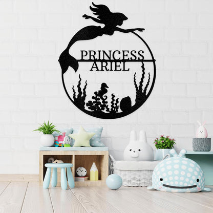 Black metal mermaid monogram wall art with "Princess Ariel" in a circular design over seaweed and a seahorse.