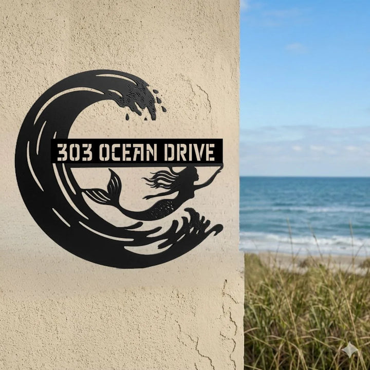 Decorative metal sign with '303 Ocean Drive' on a textured wall, beach in the background