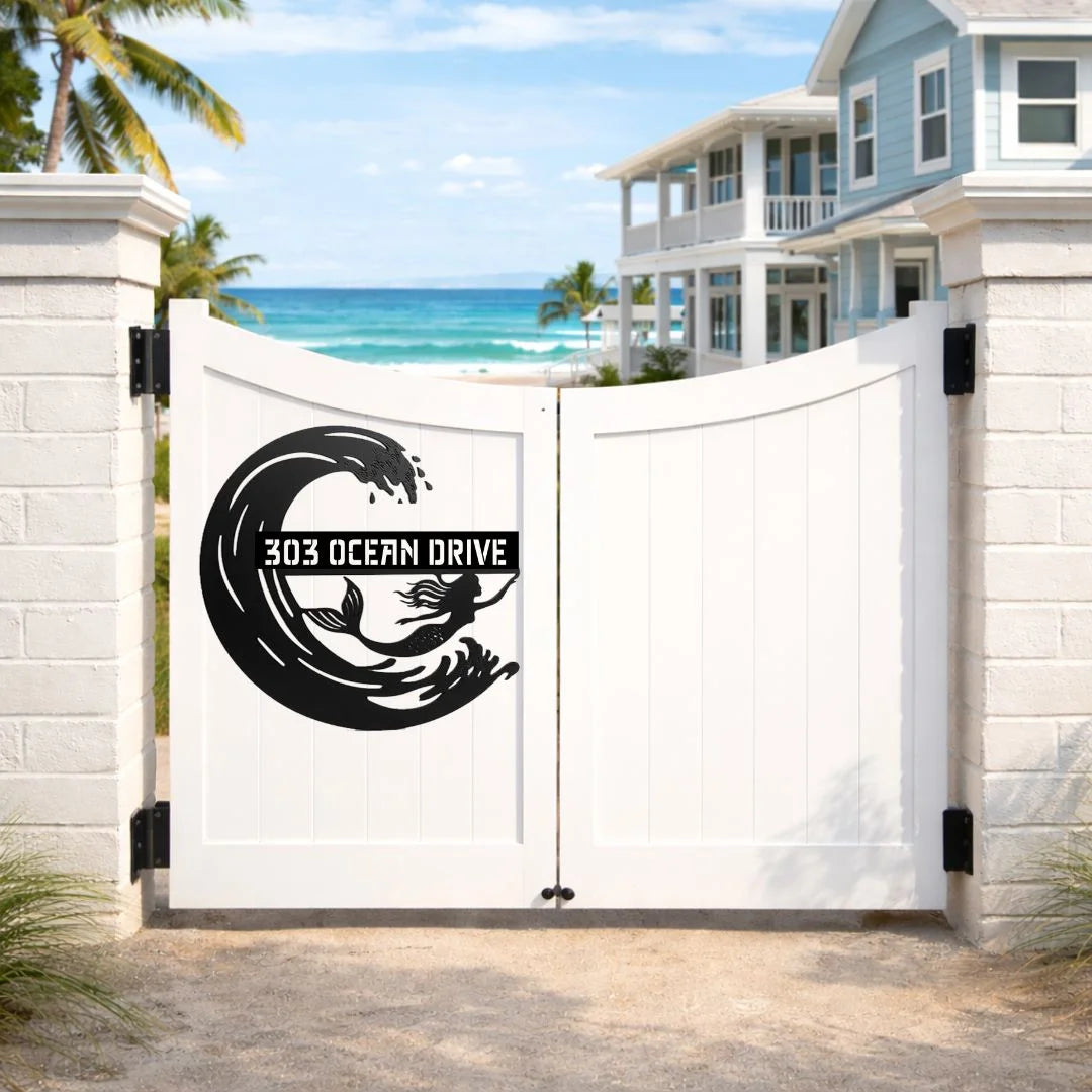 White gate with black design and text '303 Ocean Drive' in a beach setting with houses and ocean view.