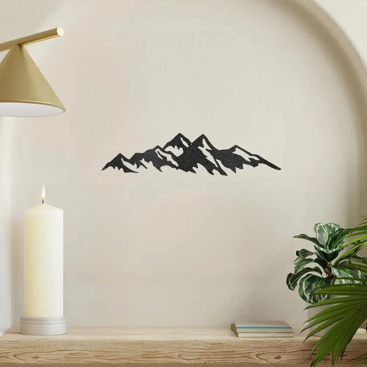 Black textured metal wall art depicting a mountain range silhouette, displayed on a cream wall.