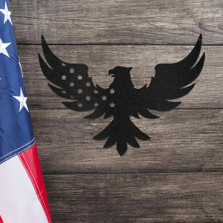 Black metal eagle wall art with stars on its wing, next to an American flag on a wooden background.