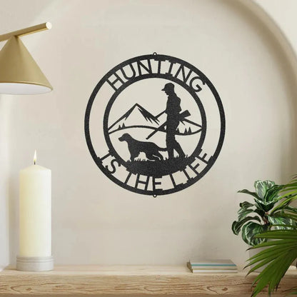 Black metal "Hunting Is The Life" wall art with hunter, dog, and mountain silhouette design.