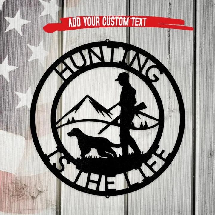 Black metal "Hunting Is The Life" wall art with hunter, dog, and mountains, on a rustic wood background.