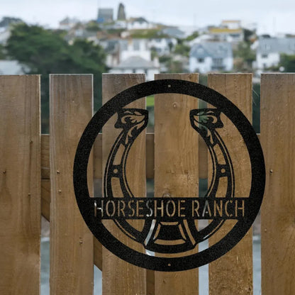 Black metal horseshoe monogram "Horseshoe Ranch" sign on a rustic wooden fence.