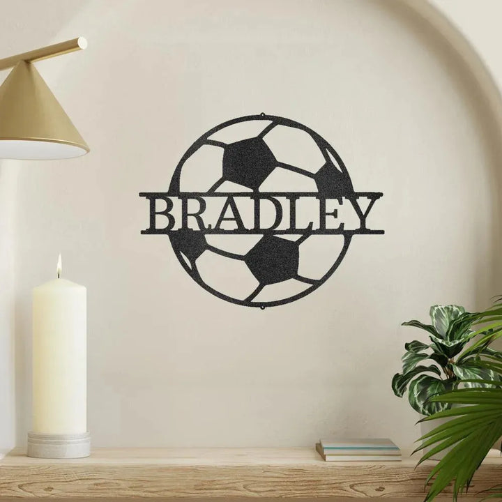 Black metal soccer ball monogram wall art with "BRADLEY" cut out, mounted on a light wall.