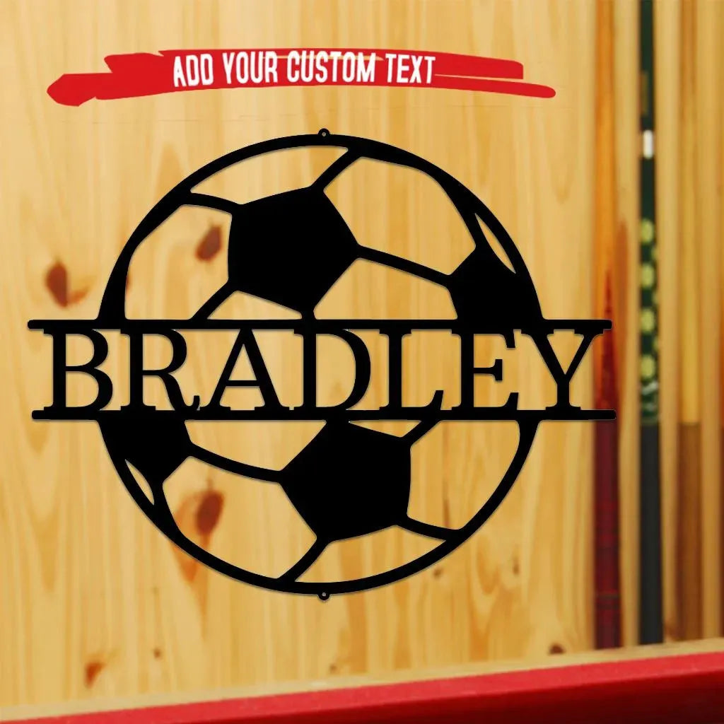 Black metal soccer ball monogram wall art with "BRADLEY" cut out, hanging on a wooden wall.