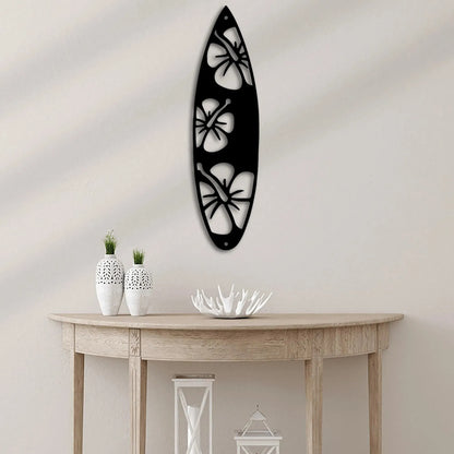 Black metal surfboard wall art with three white hibiscus flower cutouts, hanging above a wooden console table.