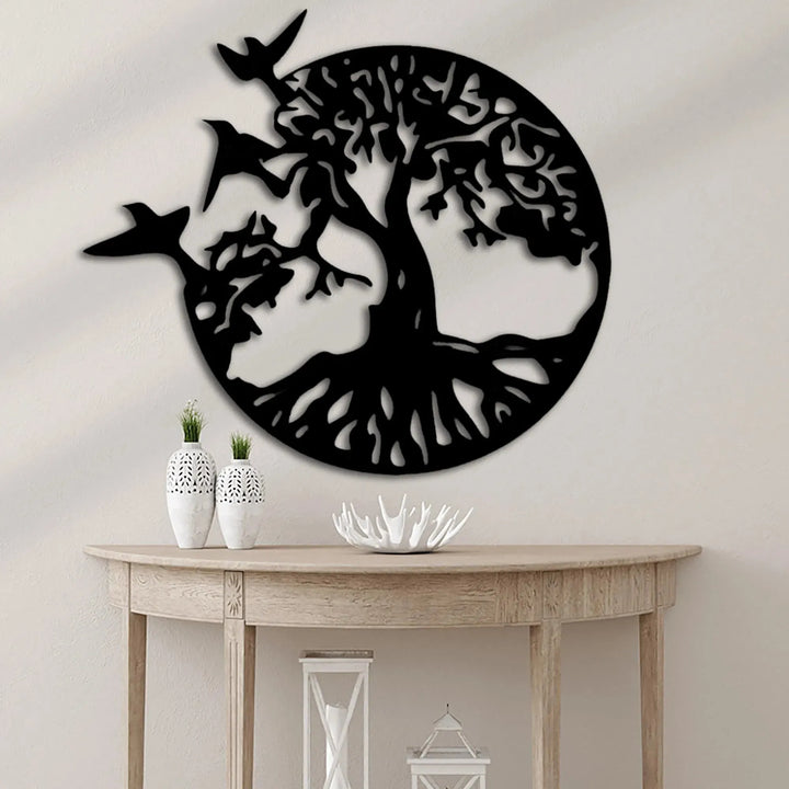 Black metal tree of life wall art with flying birds, mounted above a wooden console table.