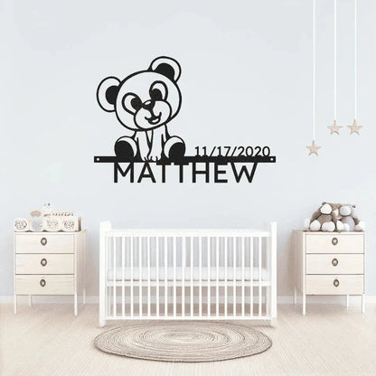 Black metal wall art featuring a teddy bear, "MATTHEW", and a birthdate above a white crib.