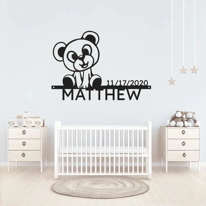 Black metal wall art featuring a teddy bear, "MATTHEW", and a birthdate above a white crib.
