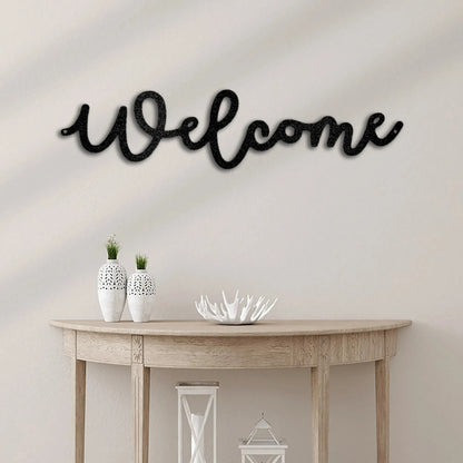 Black script "Welcome" metal wall art above a light wood console table with white vases.