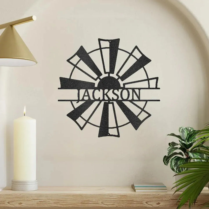 Black metal windmill monogram wall art with "JACKSON" cut out, displayed on a light wall.