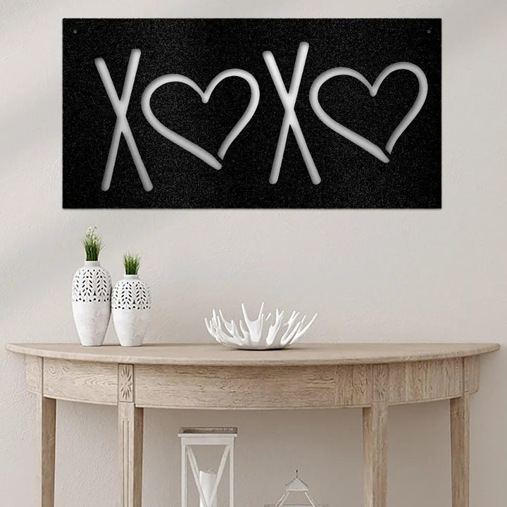 Black metal XOXO wall art with white letters and hearts, displayed above a wooden console table.