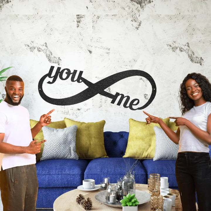 Black metal "You ∞ Me" infinity wall art above a blue sofa, displayed by a smiling couple.
